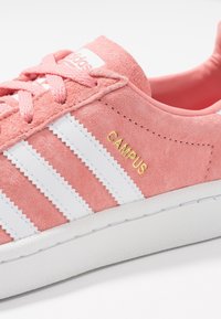 Sneaker in suede rosa con strisce bianche, dotata di un logo dorato "CAMPUS" e di una suola in gomma bianca texturizzata. I lacci sono dello stesso colore della scarpa.