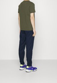 Mörkgrön kortärmad t-shirt, marinblå elastiska byxor och lila träningstrumpor med neonlysande detaljer ingår i denna avslappnade outfit.