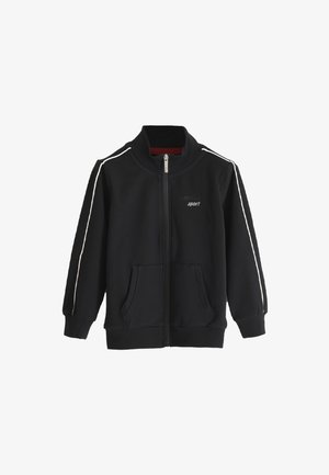 Chaqueta deportiva negra con cremallera hecha de tejido suave, que presenta rayas blancas en los laterales, dos bolsillos frontales y un cuello alto. Logo "SUPERGA sport" en el frente.