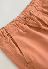 Shorts en coton orange avec une taille élastique, cordon de serrage et poches latérales, présentant une texture lisse et des détails de couture simples.