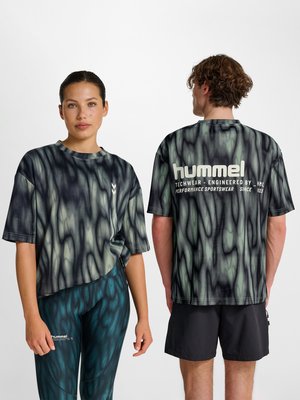 Kvinde vender fremad iført mønstret t-shirt og leggings; mand vender væk iført matchende mønstret t-shirt og sorte shorts, begge står mod hvid baggrund.