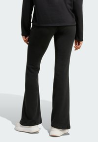 Černé rozšířené kalhoty vyrobené z měkké tkaniny, s hladkou texturou, pasem a bočními švy, doplněné o bílé tenisky.