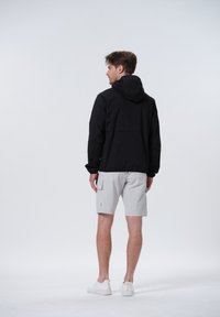 Schwarze leichte Jacke mit Kapuze, kombiniert mit hellgrauen Shorts. Die Jacke verfügt über elastische Bündchen und ein einfaches, funktionales Design.