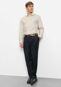 Beiges Langarmhemd mit Knöpfen, kombiniert mit dunkler, maßgeschneiderter Hose und braunen Lederschuhen, mit glatter Textur und klassischem Design.