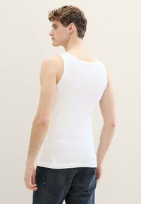 Un débardeur blanc côtelé avec un col rond et des bretelles larges, associé à un jean denim foncé, vu de dos.