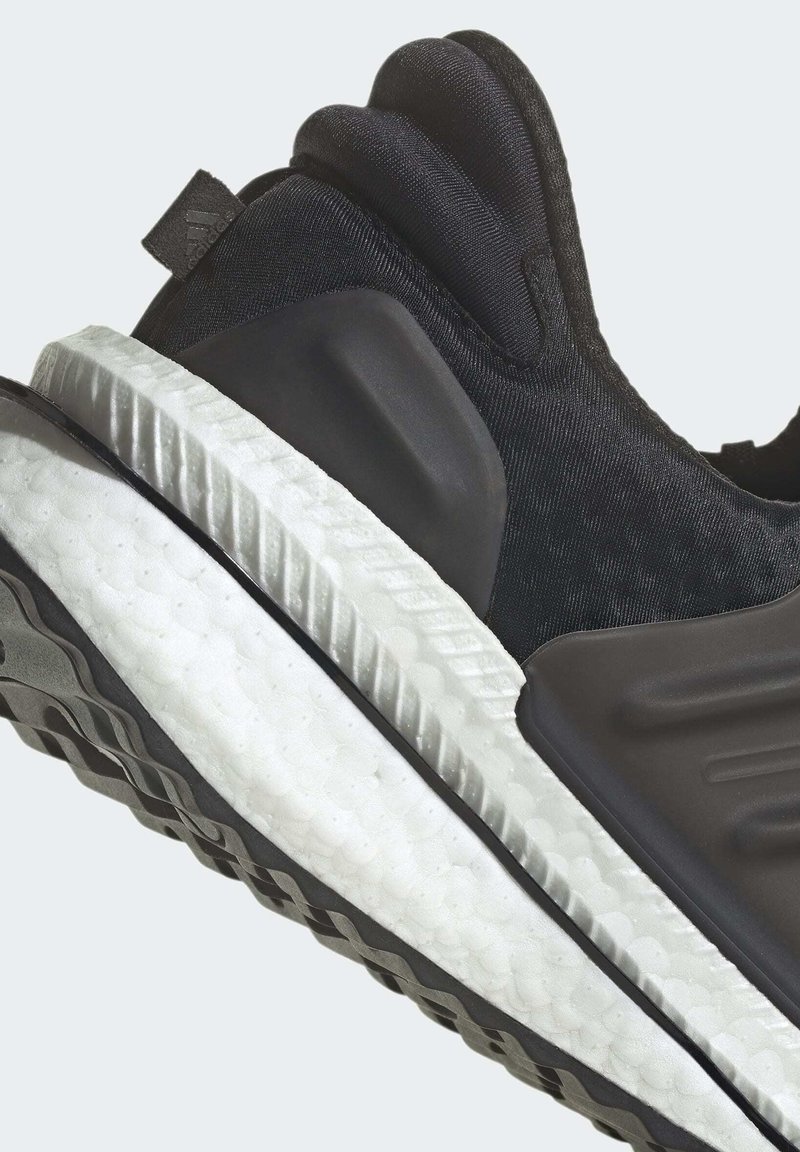 Schwarzer Sportschuh mit einer strukturierten Oberseite, einer gepolsterten weißen Sohle und einem glatten schwarzen Fersenakzent. Verfügt über ein tiefes Profil.