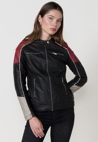 Giubbotto in pelle nera con accenti imbottiti rossi sulle spalle, dettagli in zip argentati e polsini delle maniche beige a contrasto. Presenta due tasche frontali.