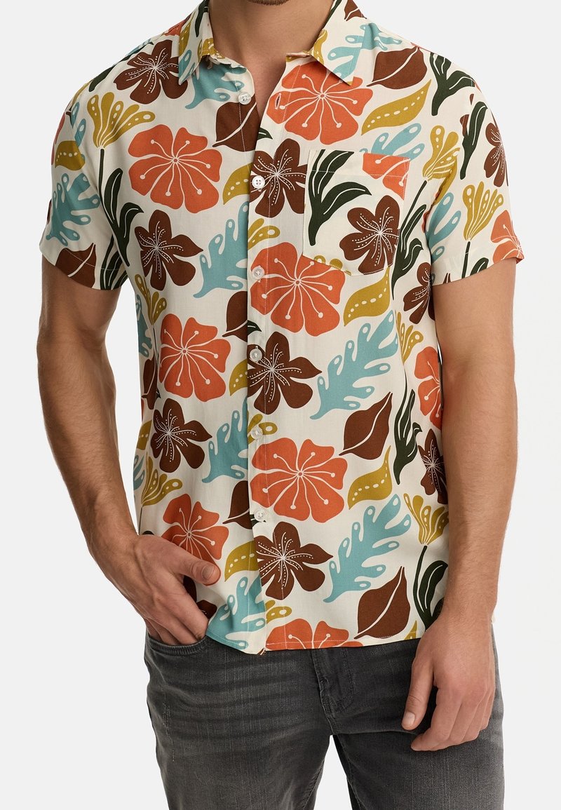 Camisa de botones de manga corta con grandes patrones florales y de hojas en naranja, marrón, verde, amarillo y azul, combinada con jeans gris oscuro.