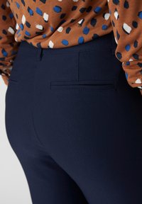 Pantaloni fitted blu realizzati in tessuto elasticizzato, con due tasche posteriori dalla texture morbida e dalla forma slanciata.
