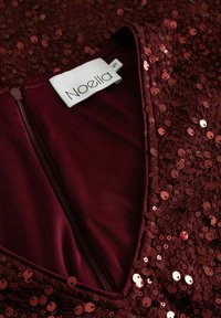 Bordo suknelė su blizgučių apdaila, V formos iškirpte ir paslėptu užtrauktuku. Etiketėje nurodyta "Noella", dydis 'S'. Tekstūruota paviršiaus detalė.