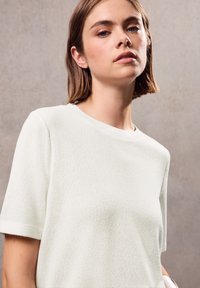 Lichtgroen, gestructureerd gebreid bovenstuk met een ronde halslijn en korte mouwen. De stof lijkt zacht en licht ademend.