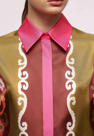 Blouse en soie avec un col rose, une bande centrale rose et des motifs artistiques en blanc sur un fond doré et marron.