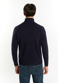Maglione blu navy a collo alto, con maniche raglan e orlo a costine. Indossato con jeans in denim blu, che mostrano un fit casual.