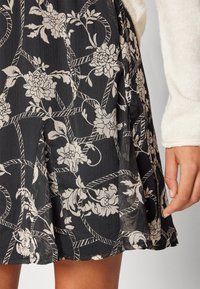 Černá květinová sukně s krémovými květinovými vzory a strukturovaným, plisovaným designem, s délkou nad kolena a lehkým materiálem.