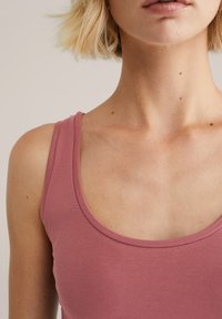Top de tirantes rosa claro con escote redondeado y tirantes estrechos. La tela es suave y ajustada, mostrando piel en la clavícula.