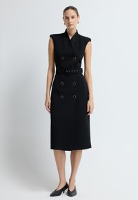 Czarna sukienka bez rękawów z dekoltem w serek, podwójnymi guzikami, paskiem w talii i złotymi akcentami. Gładka tkanina, długość do kolan.