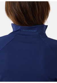 Marineblauwe sportjack met hoge kraag, met een soepele stofstructuur en het 'SWEDEMOUNT' logo op de achterkant.