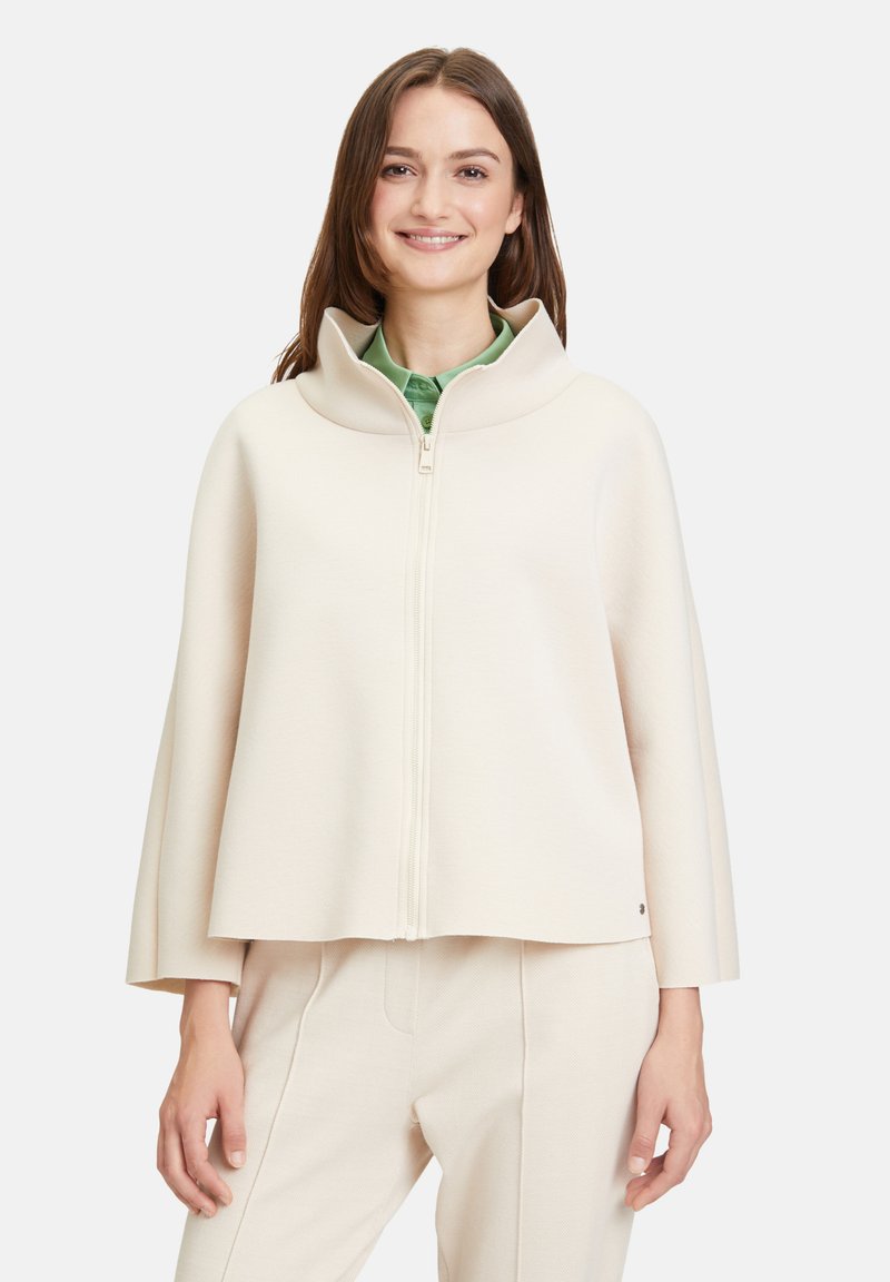 Giacca zip-up di colore crema con colletto alto, caratterizzata da una silhouette squadrata e una texture liscia. Design semplice con dettagli minimi.
