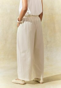 Lys beige brede bukser med elastisk talje, lavet af blødt stof. Parret med strukturerede flade sko og minimalistiske accessories.