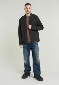 Črna bomber jakna z zadrgo na sprednji strani, kombinirana z rjavim T-shirtem, uničenimi modrimi kavbojkami in črnimi masivnimi čevlji. Prijeten in moden outfit.