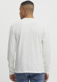 Langærmet crewneck t-shirt i lys grå, lavet af tekstureret stof. Har en lige kant og en afslappet pasform. Båret med blå jeans.