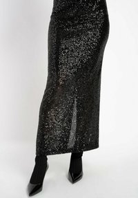 Schwarze Pailletten-Maxikleid mit taillierter Passform und seitlichem Schlitz. Kombiniert mit schwarzen spitzen High Heels und gerippten schwarzen Socken.