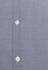 Tkanina s tmavě modrým a bílým vzorem s tkanou strukturou, obsahující dva zapínací knoflíky z bílého plastu.