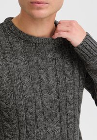 Gray knitted sweater with a ribbed crew neckline, featuring a cable knit pattern and textured details. Warm, durable, and casual design.