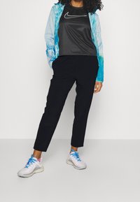 Nike sort t-shirt, blå tie-dye jakke og sorte tapered bukser. Iført hvide og blå sportssko med teksturerede såler.