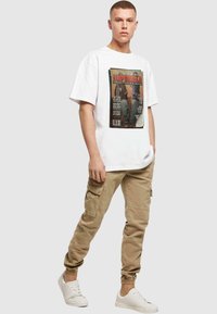 Hvid grafisk t-shirt med et stort vintage magasinprint, parret med tan cargo-bukser med lommer og hvide sneakers.
