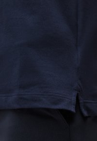 Σκούρο μπλε ύφασμα ναυτικού με υφή υφαντού, που εμφανίζει ένα τελείωμα με μια μικρή πλαϊνή σχισμή και επικαλυπτόμενο μαύρο ένδυμα από κάτω.