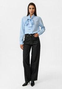 Lichtblauwe blouse met een strikjes-kraag, gecombineerd met hoge zwarte wijde jeans en zwarte puntige hakken. Gladde stoftextuur.