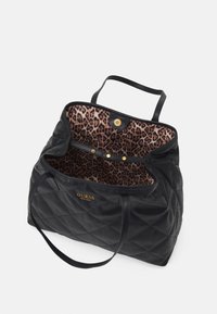 Czarna pikowana torba typu tote z dwoma solidnymi uchwytami. Wnętrze w panterkę z zapięciami na złote zatrzaski. Na przodzie znajduje się logo marki w kolorze złotym.