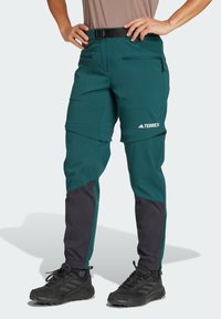 Green and black hiking pants featuring a slim fit, adjustable waistband, zippered pockets, and elastic cuffs for a secure fit.