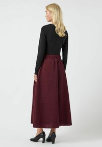 Lang bordeauxfarvet nederdel med struktureret mønster, høj talje, let flydende design, kombineret med en tætsiddende sort langærmet top og sorte højhælede sko.