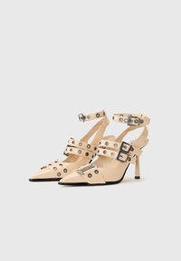 Bežiniai aukštakulniai batai su smailiais pirštais, keliomis užsegamomis juostomis su perforuotėmis detalėmis, ir elegantišku stiletto kulnu. Lygi tekstūra.