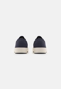 Sneakers in tela navy con design a basse, suole in gomma bianca e semplice dettaglio di cucitura. La vista posteriore mostra il tallone arrotondato e i lacci piatti.