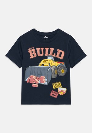 Tengerészkék ing sárga rakodóval, aki piros téglákat visz, felirat: "ÉPÍTSÜNK!", figyelmeztető és kerülőút táblák, valamint egy Tonka jelvény.