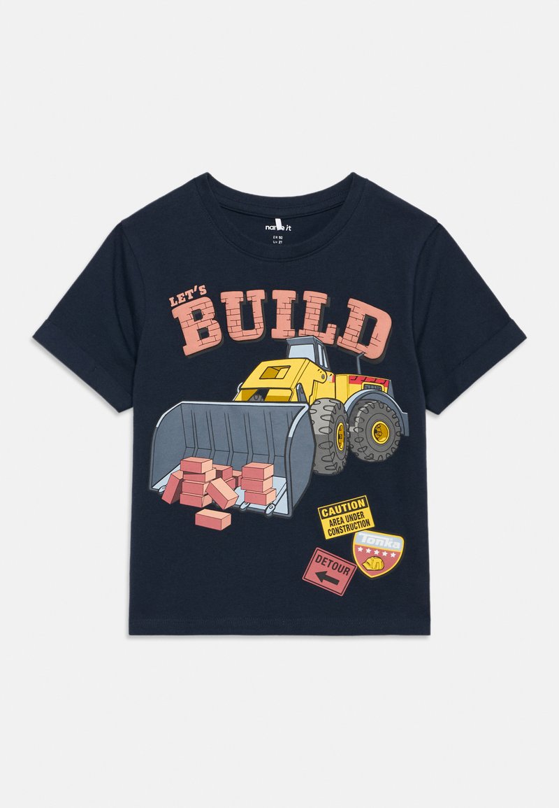 Μπλε πουκάμισο με κίτρινο φορτωτή που μεταφέρει κόκκινα τούβλα, κείμενο "ΑΣ ΟΙΚΟΔΟΜΗΣΟΥΜΕ", πινακίδες προσοχής και παράκαμψης, και σήμα Tonka.