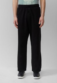 Schwarze, lässig geschnittene Hose mit elastischem Bund und Kordelzug; glattes Material und gerade Beine; kombiniert mit schwarzen Sneakern.