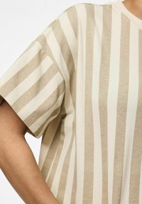 T-shirt a maniche corte a righe beige e crema, realizzato in morbido cotone, con scollo a girocollo e cuciture visibili lungo le maniche.