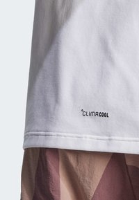 Bílá bavlněná tričko s logem "CLIMACOOL" v černé barvě. Viditelné švy na lemu, kombinované se vzorovanou tkaninou v jemných barvách dole.