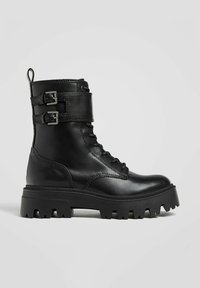 Črn usnjen gležnjar z dvema nastavljivima zaponkama, okroglo konico, debelim gumijastim podplatom in sprednjim vezalnim delom. Gladek tekstura in trdna zasnova.