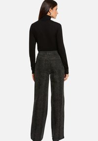 Un pull à col roulé noir associé à un pantalon large taille haute gris foncé avec un motif serpent discret et des poches arrière.