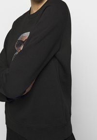 Svart sweatshirt med en texturerad design och en subtil mönstring. Den har en rund hals och ribbad nederkant och ärmar för en passande look.