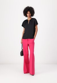 Zwarte blouse met korte mouwen en een sleutelgatenontwerp, gecombineerd met fuchsia hoge taille flared broeken. Accessoires zijn onder andere een kleine zwarte handtas.