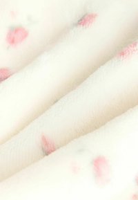 Miękki, pluszowy koc w kremowym kolorze, z małymi różowymi i zielonymi wzorami kwiatowymi. Tekstura wydaje się puszysta i ciepła.