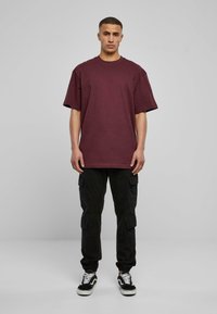 Burgundské oversized tričko s krátkými rukávy, spárované s černými cargo kalhotami s bočními kapsami a černobílými teniskami.