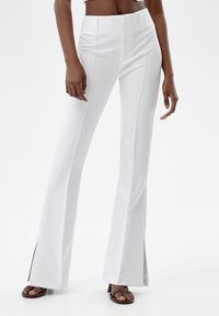 Vita utställda byxor med hög midja, med framficksdetaljer och slitsar i fållen, tillverkade av ett glatt material.