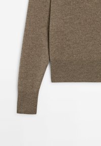 Pull marron avec un col et des poignets côtelés, fabriqué en matériau doux, présentant une coupe droite et une texture minimale.